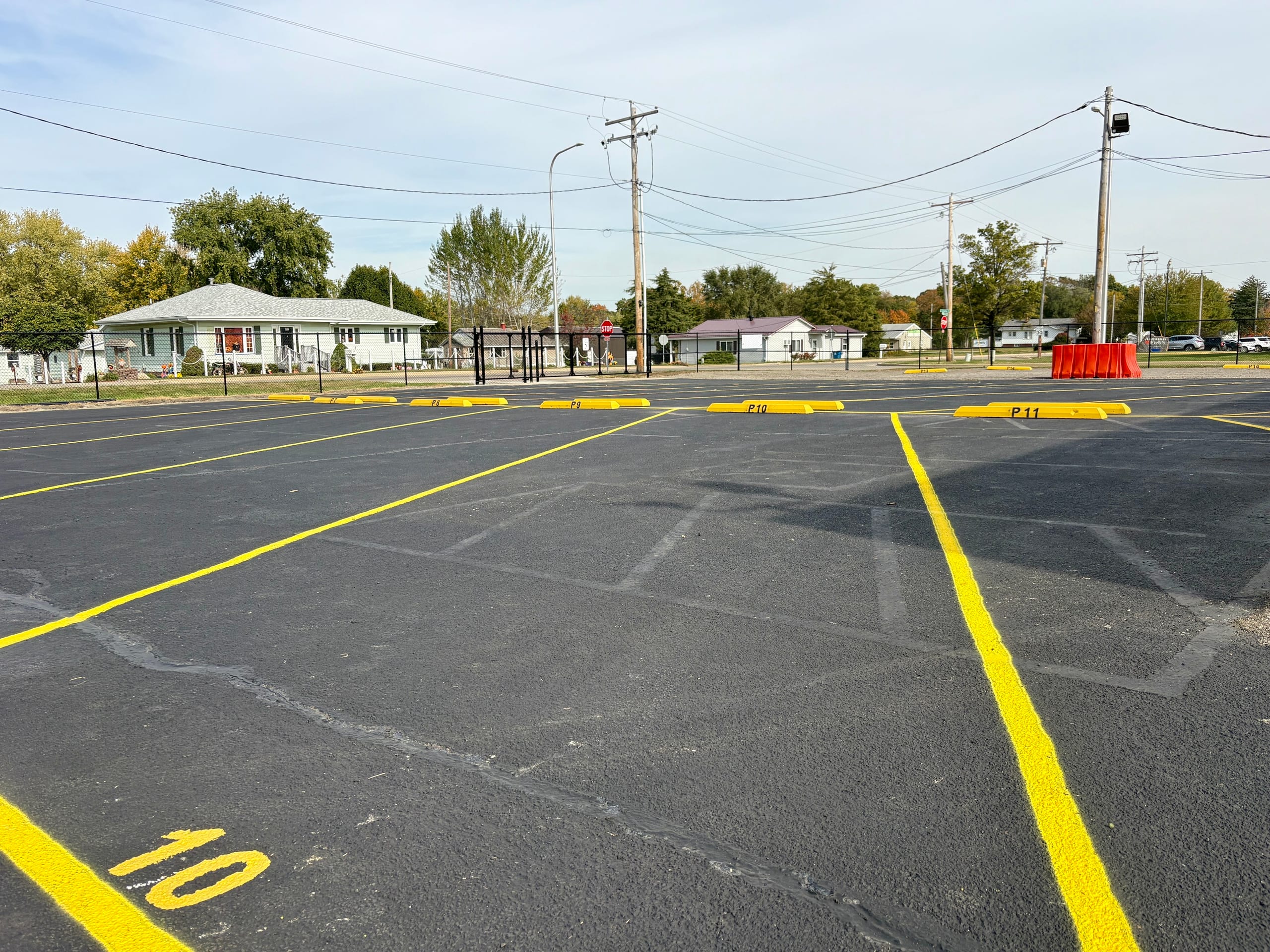 Outdoor parking space 10 painted in yellow on fresh black asphalt with wheel stops and a fenced perimeter
