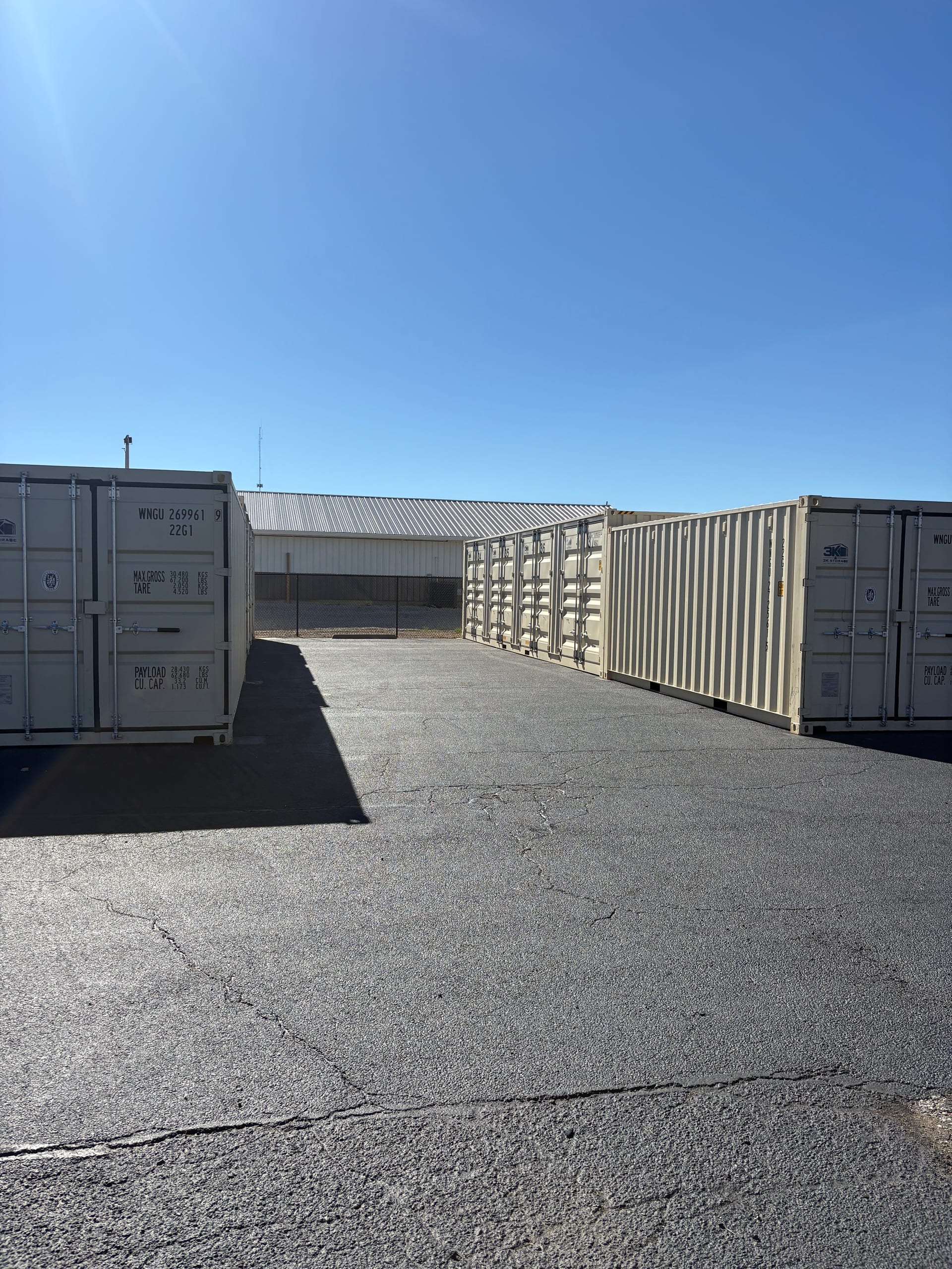 Rows of 3k Storage containers on a hard-surface paved lot with a warehouse building behind them