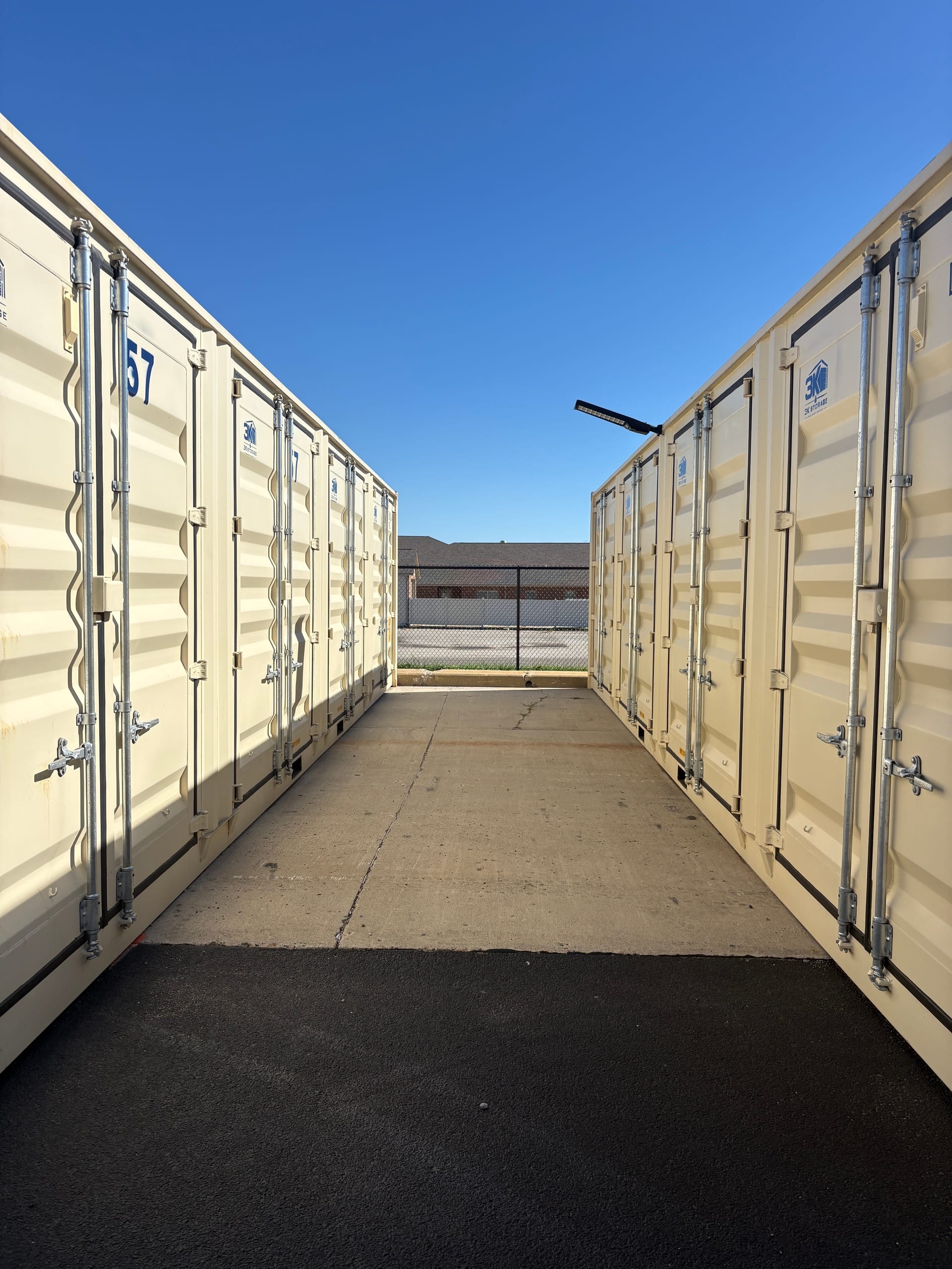Paved aisle between two rows of cream 3k Storage units under a clear blue sky